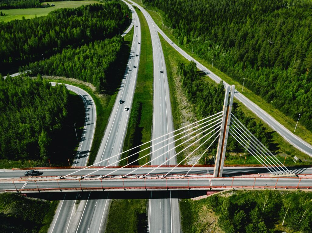 Aerial top view of cable-stayed Suspension bridge and Highway road with green forests in Finland.