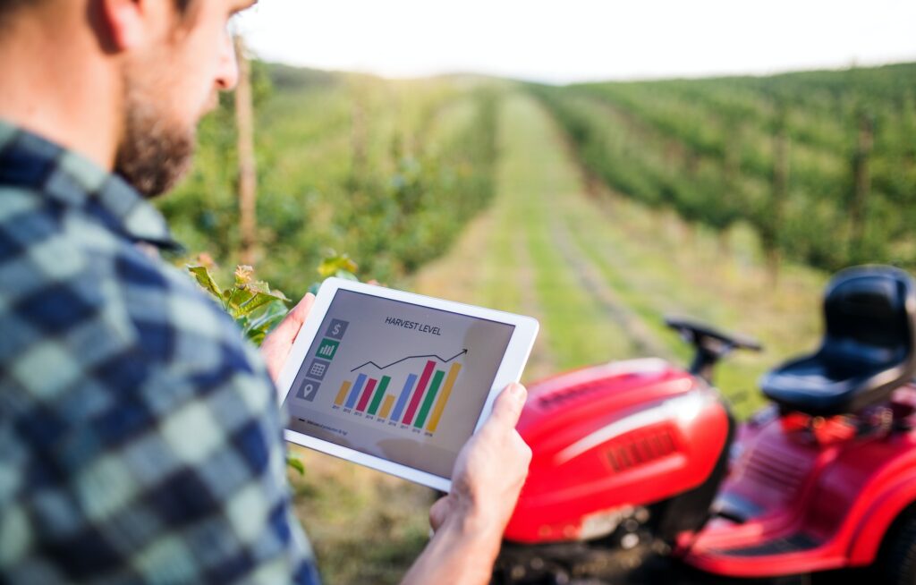 A mature farmer with tablet standing by mini tractor outdoors in orchard