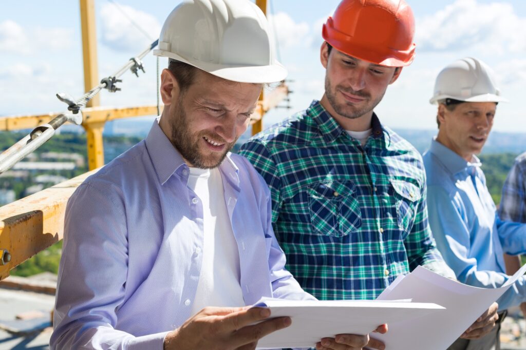 Architect And Builders Looking At Buiding Plan Blueprint Wearing Hardhat While Meeting On