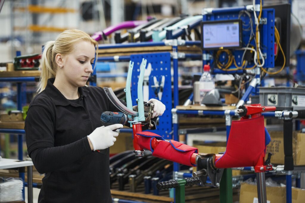 Female skilled factory worker assembling a bicycle handling the brakes assembly and part of the