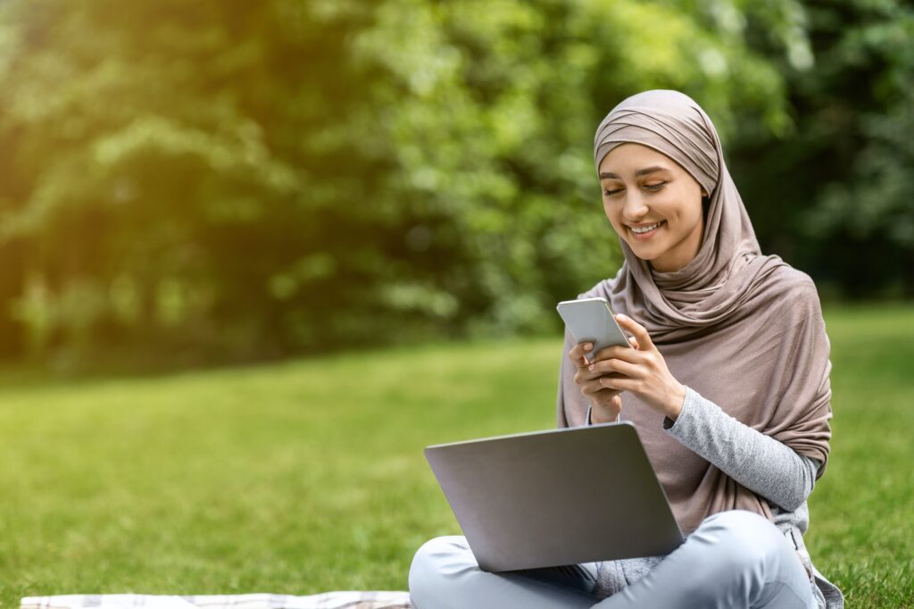 Muslim woman with laptop using mobile phone