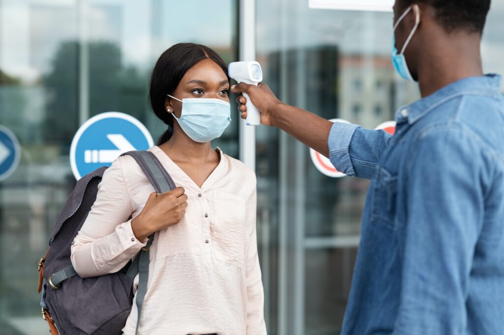 Airport Worker Checking Black Female Passenger's Temperature With Electronic Thermometer After