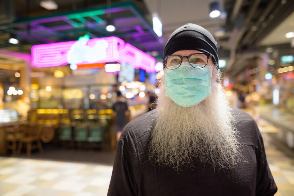 Mature bearded hipster man thinking with mask for protection from corona virus outbreak at the mall